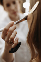 Makeup artist applying blush or highlighter to model face. Close-up vertical
