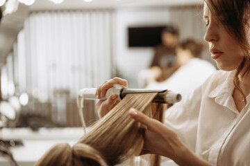 Make-up artist hairdresser creates hairstyle for model, uses hair curling iron
