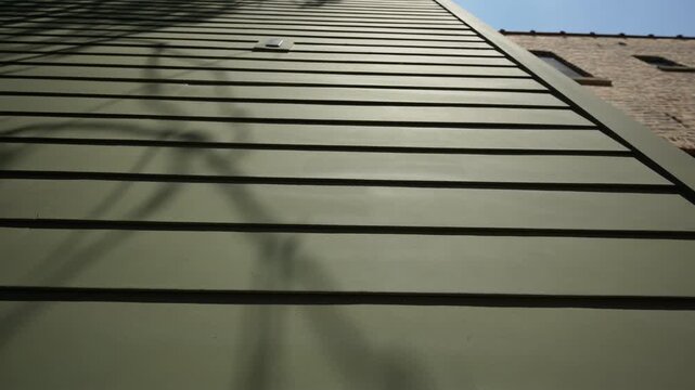 Wide view of green siding of the house wall with modern panels, providing a sleek and classic exterior look on sunny day. move camera view