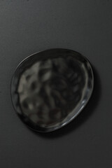Minimalist black ceramic plate, placed on a dark textured background