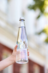 Hand holding clear glass water bottle outdoors on a sunny day.