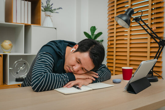 tired man with tablet and wireless earbuds at home office