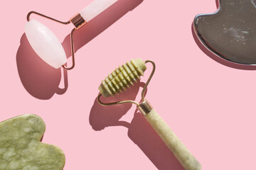 Skincare tools on pink background with jade roller and facial massager for beauty regimen.