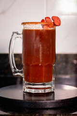 Mexican michelada drink is garnished with chili powder and tamarind candy, sitting on a black coaster
