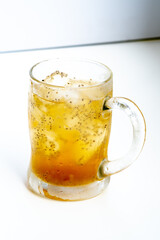 A close-up of a refreshing iced tea in a frosted glass mug. The cold beverage is infused with healthy chia seeds (Salvia hispanica) and ice cubes, shot in a bright, high-key style.