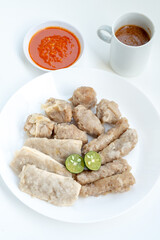 A plate of Siomay, a popular Indonesian street food, featuring steamed fish dumplings, tofu, and fish cakes with sliced lime. A bowl of chili sauce and a mug of peanut sauce are also visible.