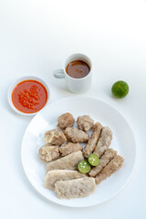 A plate of Siomay, a popular Indonesian street food, featuring steamed fish dumplings, tofu, and fish cakes with sliced lime. A bowl of chili sauce and a mug of peanut sauce are also visible.