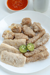 A plate filled with various types of steamed Indonesian siomay, including fish dumplings and stuffed tofu, served with two slices of lime.