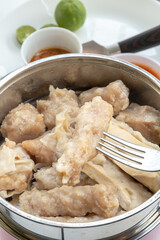 A fork is lifting a piece of traditional Indonesian siomay from a steamer pot, with various other siomay pieces visible around it.