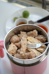 A fork is lifting a piece of traditional Indonesian siomay from a steamer pot, with various other siomay pieces visible around it.