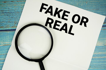 Fake Or Real text written on notepad with magnifying glass flat lay on wooden background