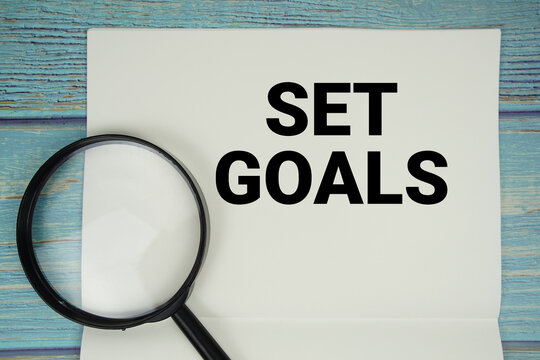 Naklejki Set Goals text written on notepad with magnifying glass flat lay on wooden background