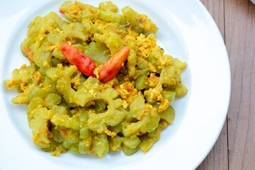 A close-up of Tumis Pare, a popular Indonesian home-cooked dish. Slices of bitter melon (Momordica charantia) are stir-fried with scrambled egg and spices, garnished with red chilies.