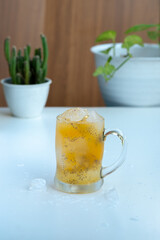 A sweating glass mug of iced orange juice with hydrating basil seeds (biji selasih) sits on a rustic wooden plank, featuring a bright, tropical, and refreshing summer look.
