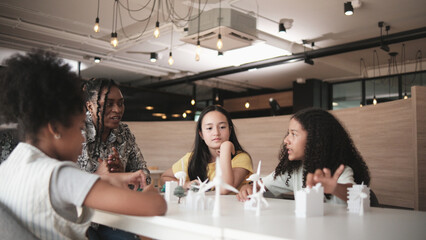 Black female teacher teaches and instructs primary girls group students, clean energy lesson at learning table in science classroom, discusses experiment knowledge for children of elementary school.