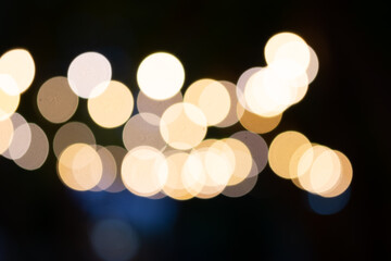 A blurry, abstract image of soft, round lights in a bokeh effect, with warm yellow and white tones on a dark background.