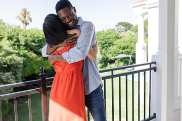 Couple embracing on balcony, enjoying sunny day at outdoor wedding venue