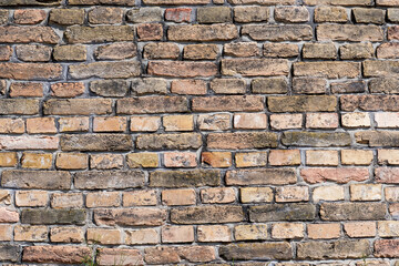 A textured brick wall is made from old, weathered bricks in various shades of brown and tan