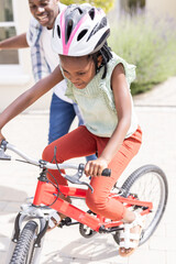 Father supporting African American child riding bicycle outdoors, both smiling