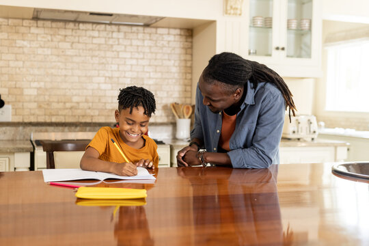African American father helping son with homework at kitchen table, both smiling