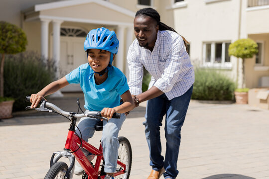 African American father teaching son to ride bicycle outside, both enjoying moment - Powered by Adobe
