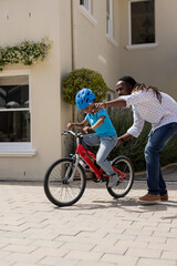 Father teaching son to ride bicycle outside home, encouraging and supporting him