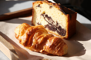 Croissant and marble cake rest on a wooden tray in sunlight