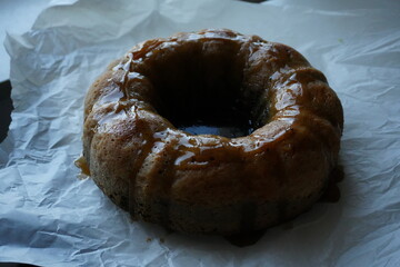 Homemade bundt cake with glaze on parchment paper, rustic autumn dessert near window, cozy seasonal baking symbolizing warmth, comfort, and homemade tradition.