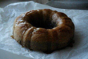 Homemade bundt cake with glaze on parchment paper, rustic autumn dessert near window, cozy seasonal baking symbolizing warmth, comfort, and homemade tradition.