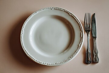 Empty white plate and cutlery on a pale peach background