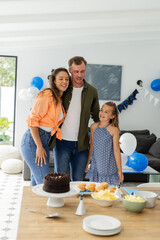 Family celebrating birthday at home with cake and balloons, smiling together