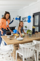 Mother and daughter setting table for birthday celebration at home, smiling happily