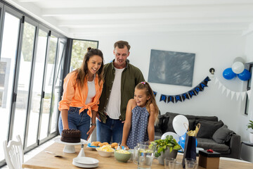 Family celebrating birthday at home, smiling and looking at cake on table
