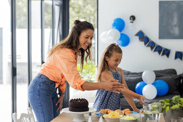 Mother and daughter preparing birthday table with cake and decorations at home