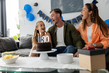 Family singing around birthday cake with lit candles, celebrating joyfully at home