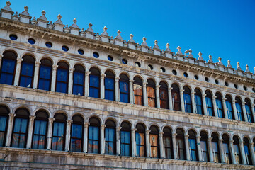 Obraz premium Historic building facade with rows of arched windows and decorative elements against blue sky. Concept of architecture, travel and Italian cultural heritage.