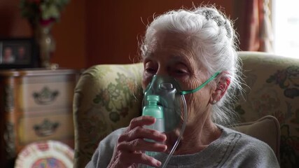 Frail elderly woman in an armchair using a nebulizer mask for breathing assistance at home - Powered by Adobe