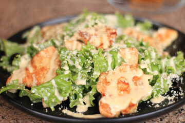 Close-up of Caesar salad with grilled chicken, romaine, parmesan on black plate.