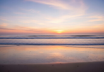 Peaceful ocean sunset with gentle waves reflecting on wet sand