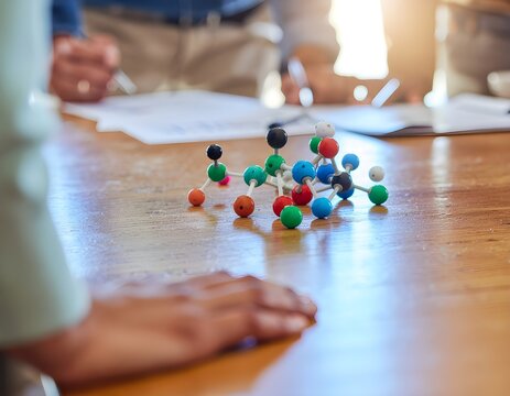 Molecular model on a wooden table with people in the background during a meeting. - Powered by Adobe