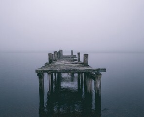 Foggy, weathered wooden pier extends into a still lake
