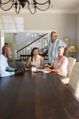 Seniors discussing plans around table, using tablet and notebook at home
