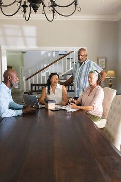 Seniors discussing plans around table, using tablet and notebook at home