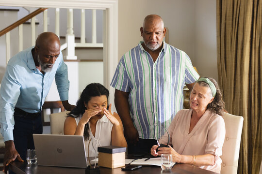 Discussing finances at home, senior group looking concerned around laptop and documents