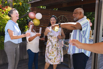Celebrating outdoors, seniors pouring champagne and laughing with friends in garden