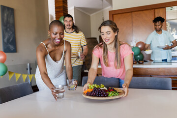 Friends setting table with fruit platter and drinks, preparing for indoor gathering