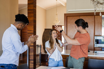 Friends celebrating success at home, clapping and smiling with excitement
