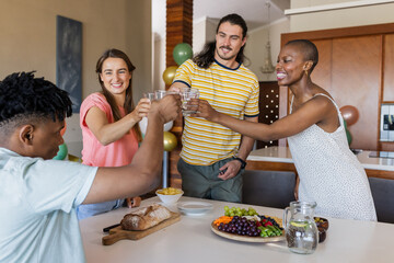 Friends toasting with water glasses around table with fruit platter in kitchen