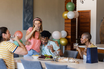 Friends celebrating at home, enjoying drinks and snacks around dining table