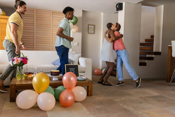 Friends celebrating at home, hugging and smiling with balloons and cake on table